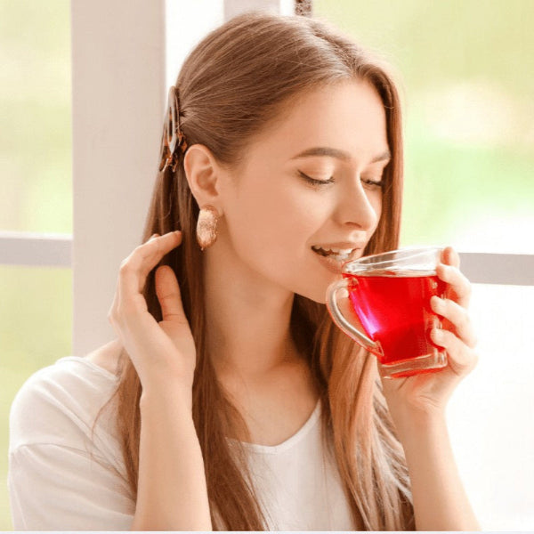 Woman drinking from a cup of red tea in a bright room with large windows.