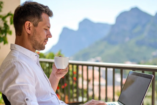 Man using a laptop on a balcony with mountains in the background