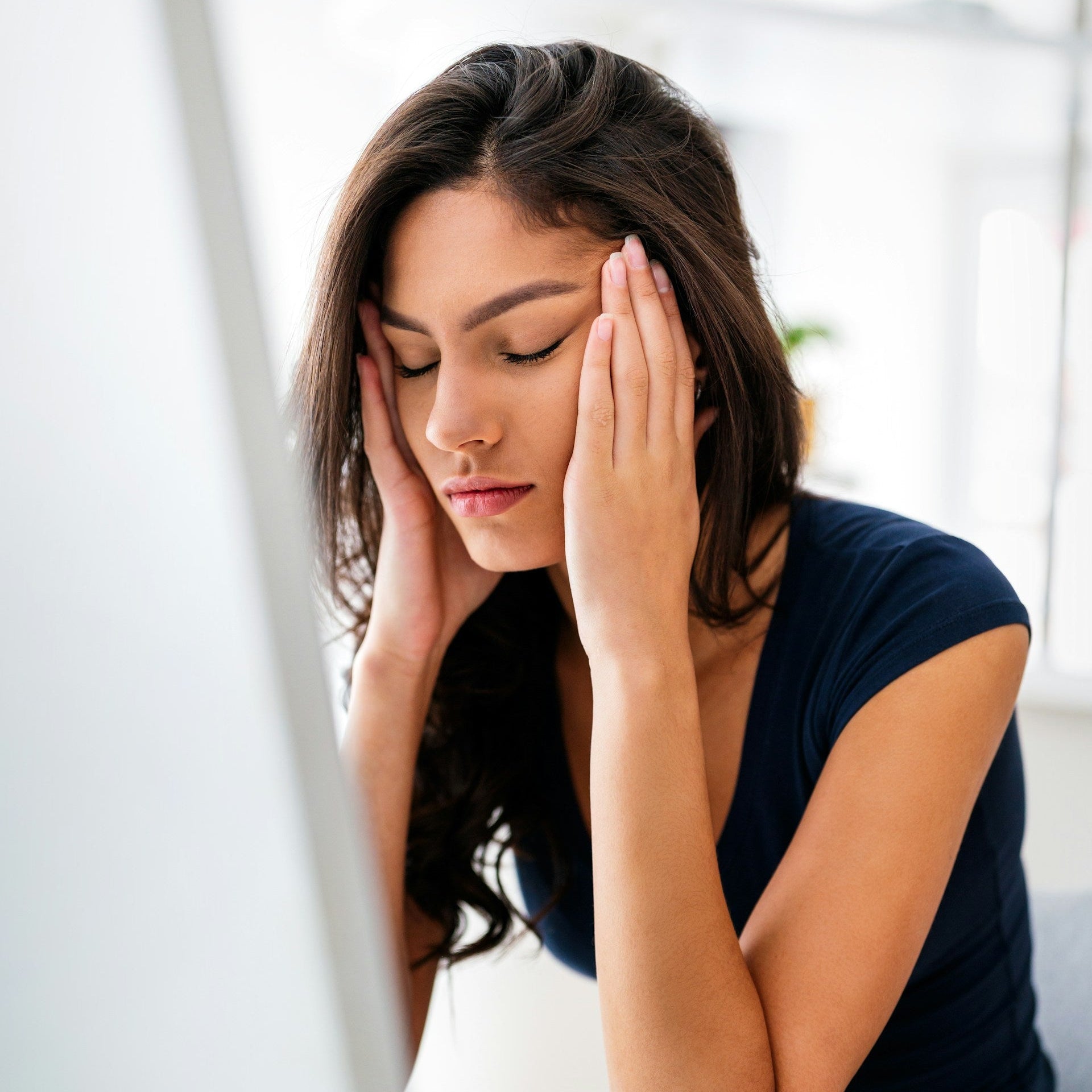 Woman with head in hands in front of a computer screen