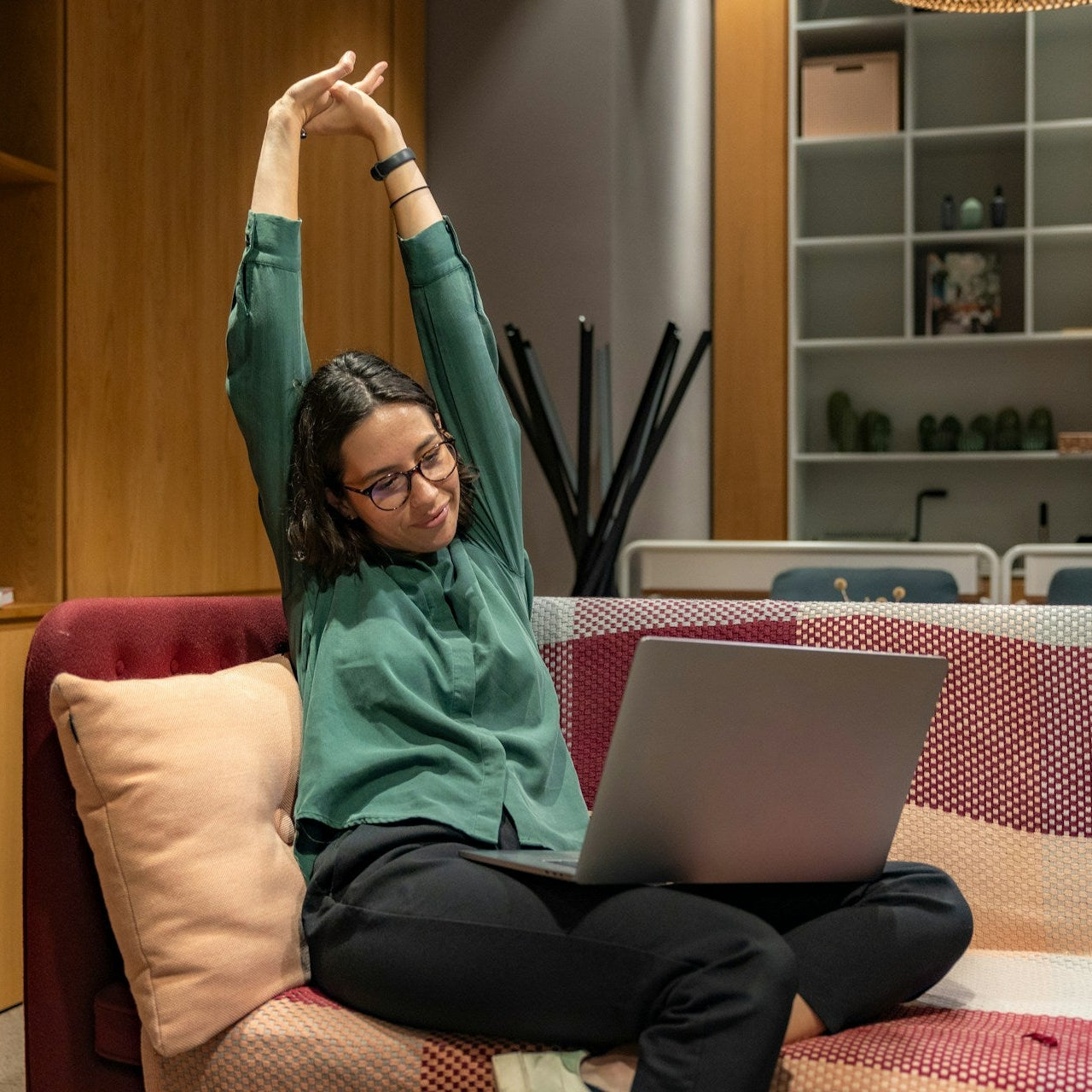 Person sitting on a couch with a laptop, stretching in a home setting